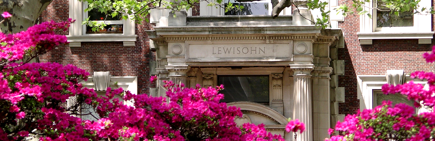 Close-up of Lewisohn Hall, a brick building with 2 columns at the entrance, surrounded by fuchsia flowers