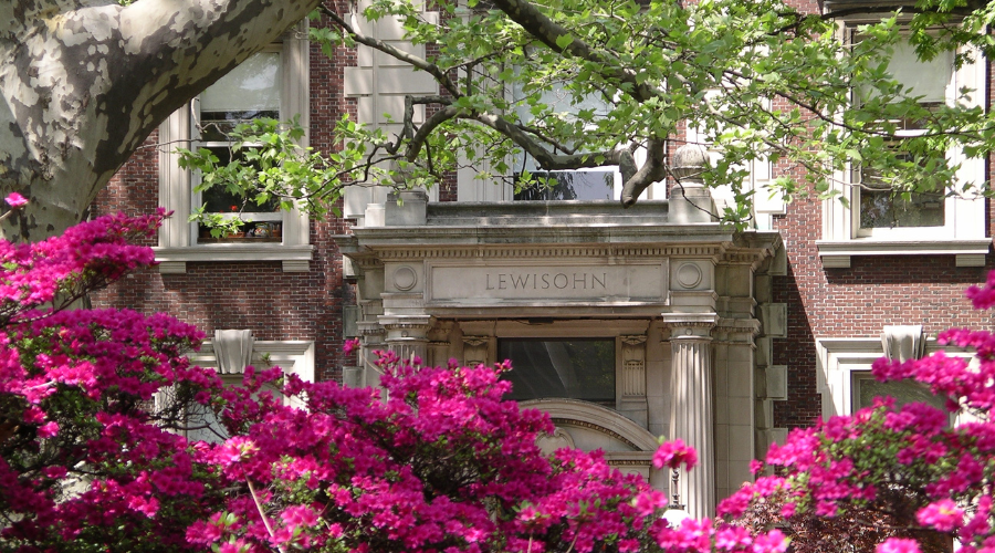 Front of Lewisohn Hall surrounded by green tree canopy and pink flowers