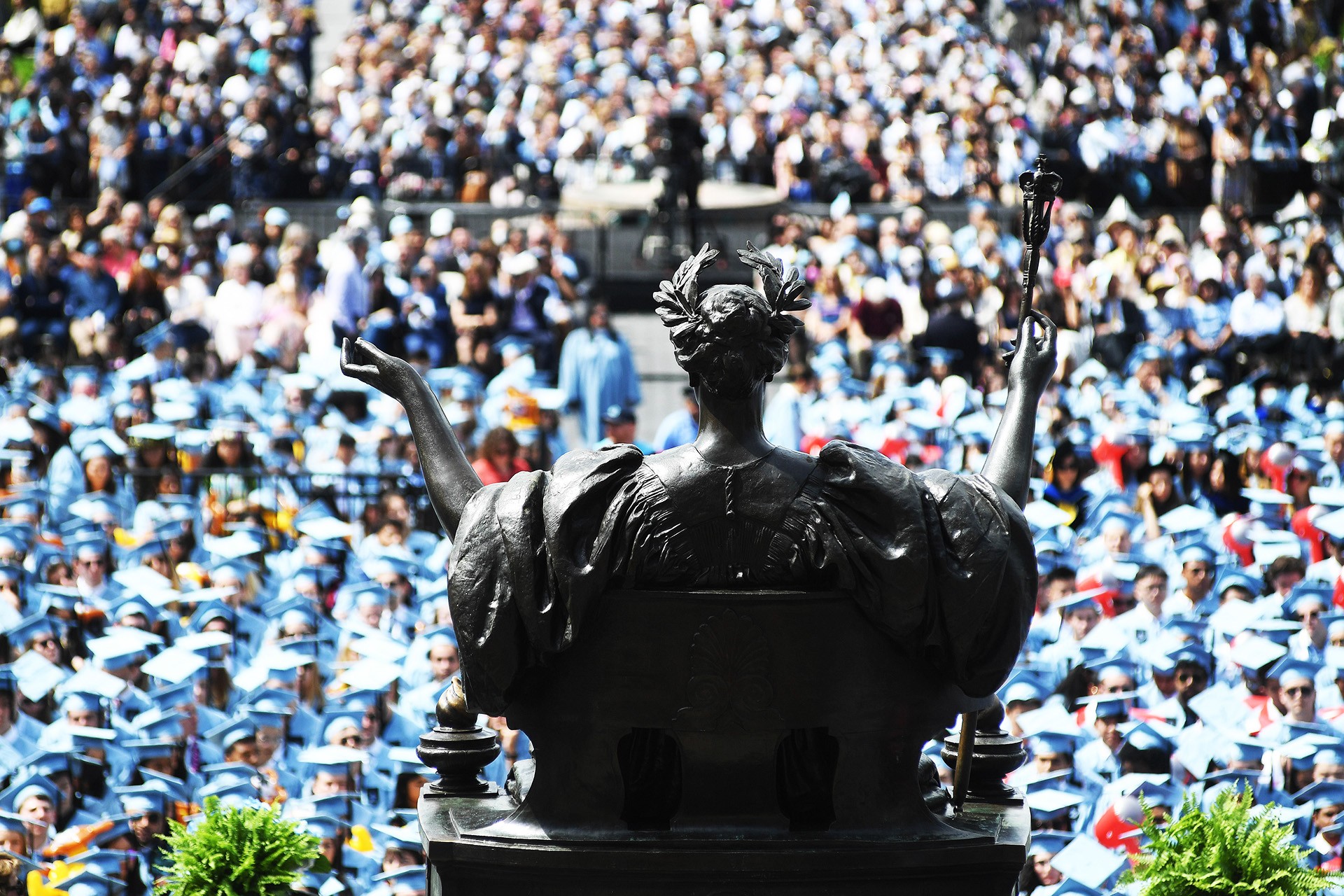 Photo taken of graduates at Commencement from behind the Alma Mater statue