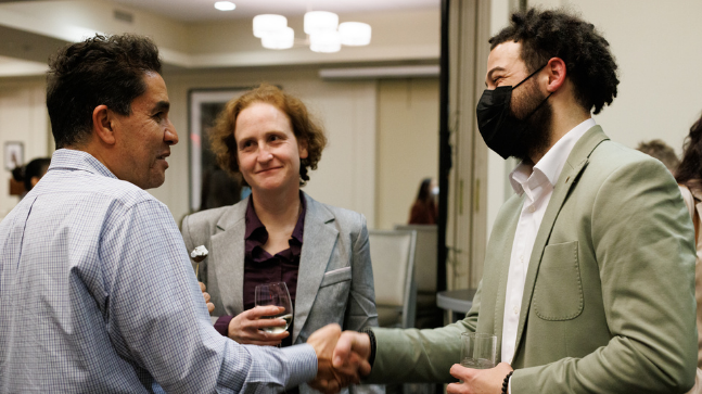 Three students chat and shake hands.