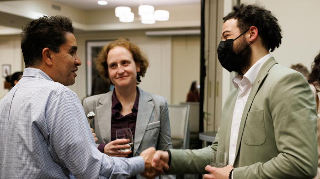 Three students chat and shake hands. 