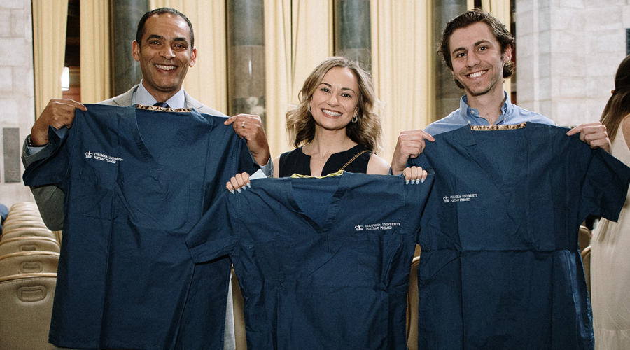 Three members of the Postbac Premed Class of 2023 holding their scrubs