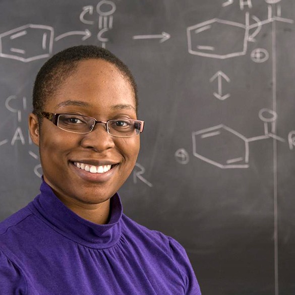 Postbac premed students stands in front of a chalkboard with science formulas.