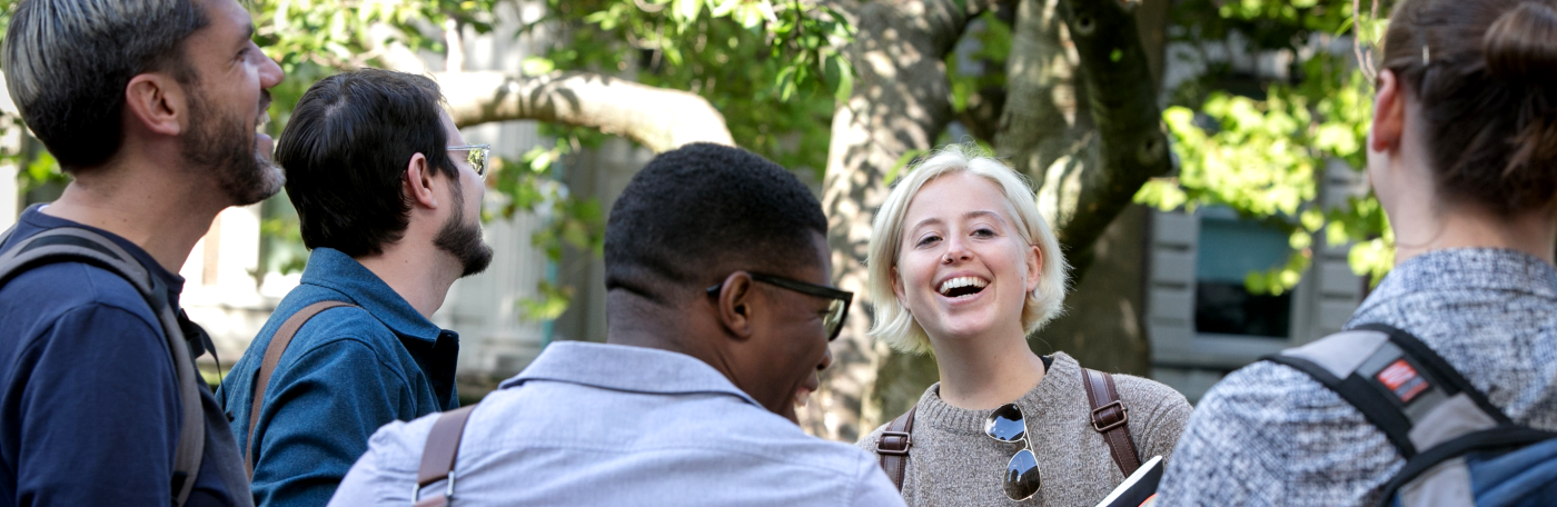 Group of men and women laughing outside with tree behind them