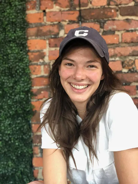 GS student Dorothee Grant smiles for a phot in front of a brick wall backdrop. 