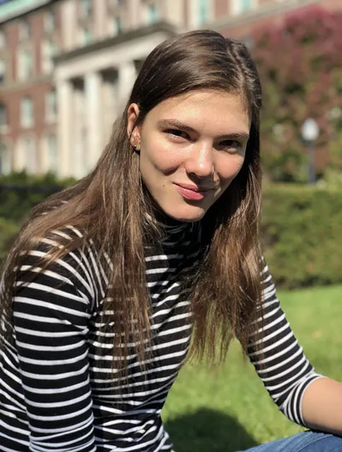 GS student Dorothee Grant poses for a photo sitting on the grass in front of a Columbia building