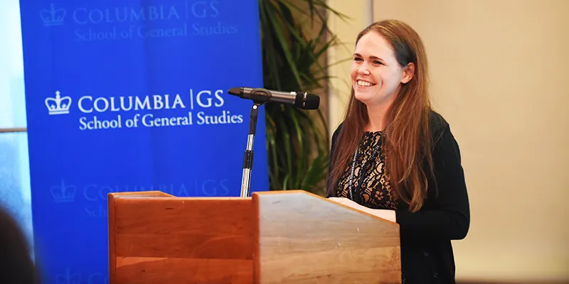 Elizabeth Ross speaks to dinner attendees with a Columbia GS stanchion in the background 