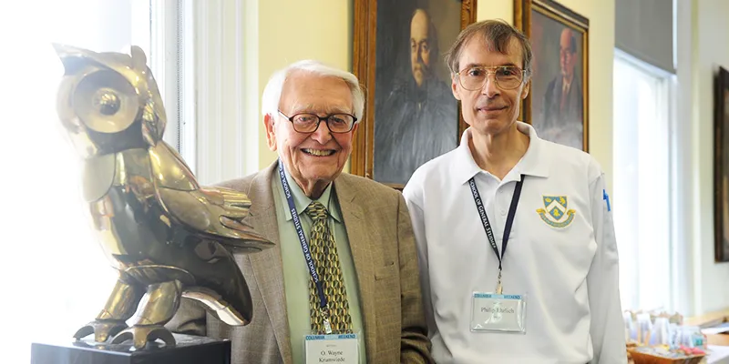Two GS alumni pose for a photo next to the Owl sculpture