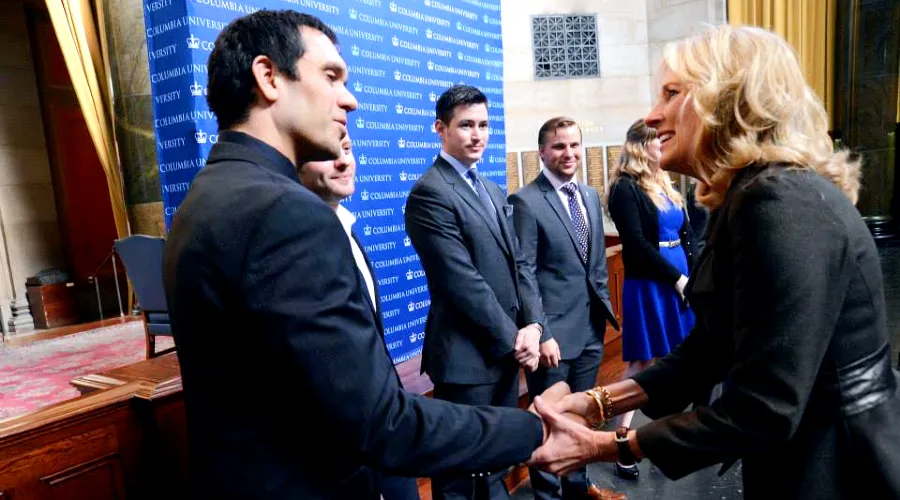 Dr. Jill Biden shakes hands with a student, with 4 additional students standing in the background