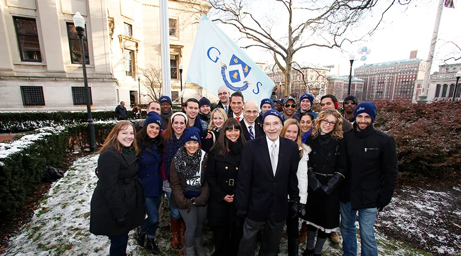 A group of GS students and alumni pose with Dean Awn in front of the GS flag