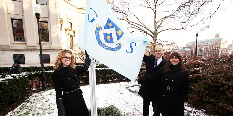 Three people pose with the GS flag as it's raised up the pole for the first time