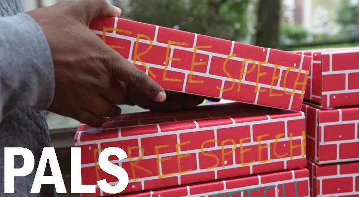 A hand stacking cardboard bricks reading "free speech"