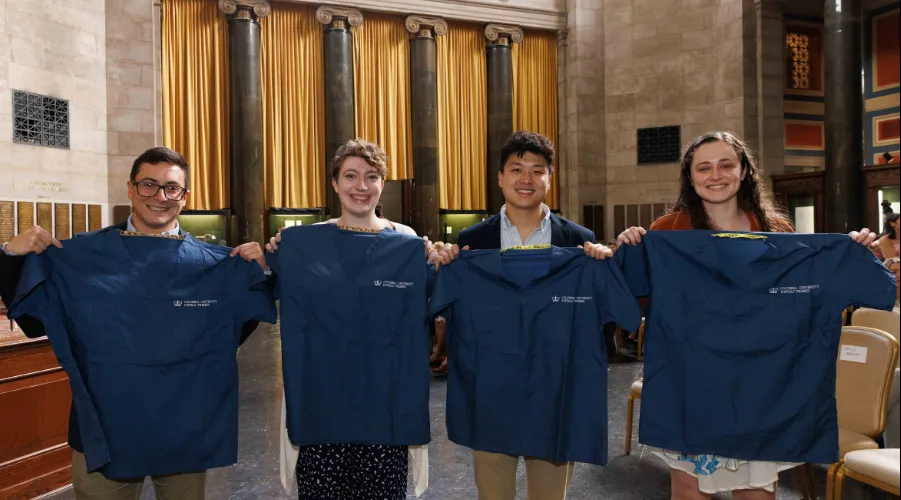 Four graduates hold up their Columbia scrubs. 