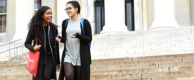 Two students talking as they walk down a set of marble steps on campus.