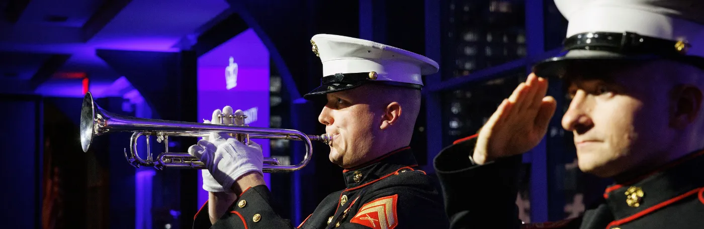Two veterans in dress uniforms, one playing a trumpet, one saluting, at the annual Columbia Military Ball 